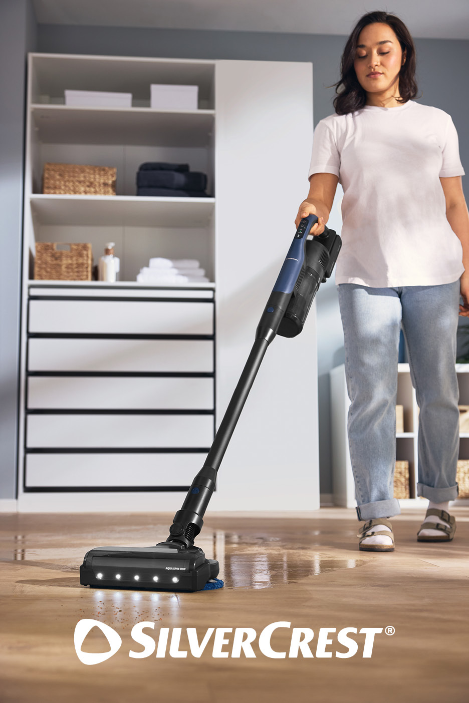 Donna pulisce il pavimento in legno con un aspirapolvere senza fili, armadio sullo sfondo.