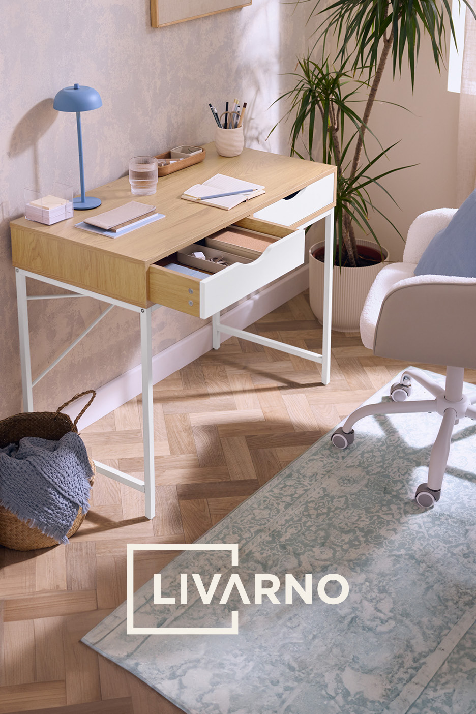 Scrivania in legno chiaro con cassetti aperti, lampada blu e sedia da ufficio in un ambiente domestico.