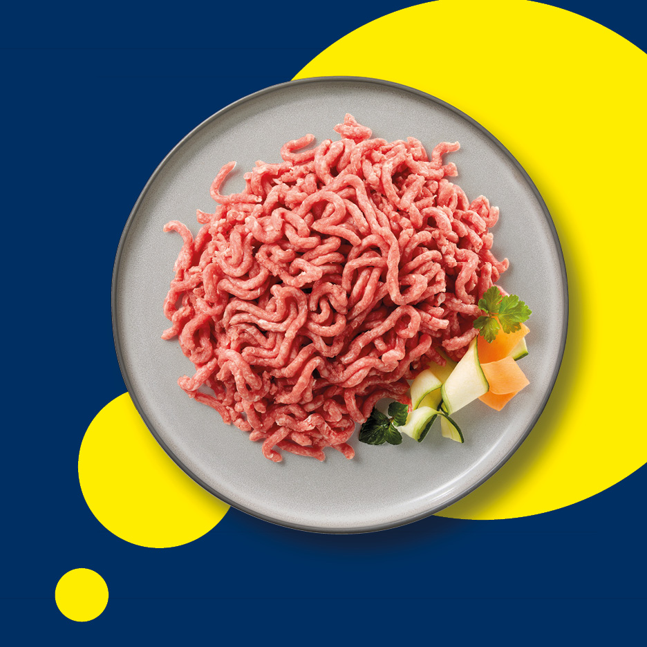 Carne macinata su un piatto grigio con contorno di verdure su sfondo blu e giallo.