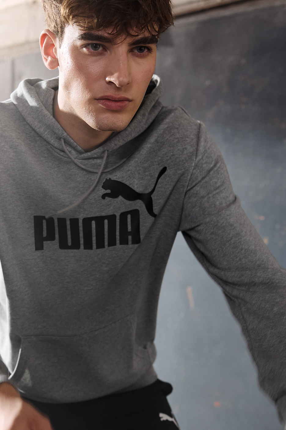 Un uomo indossa una felpa con cappuccio grigia con il logo Puma nero.