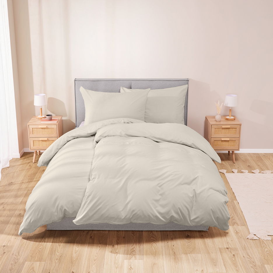 Un letto con testiera grigia e biancheria da letto color crema, affiancato da comodini in legno.