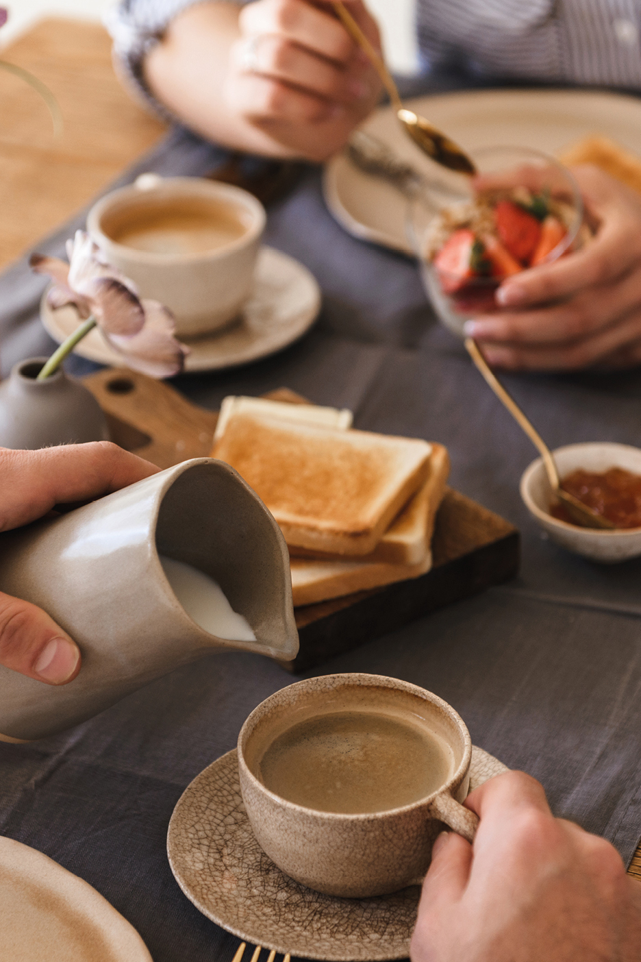 Una persona versa il latte nel caffè mentre un'altra mangia yogurt con fragole e toast.