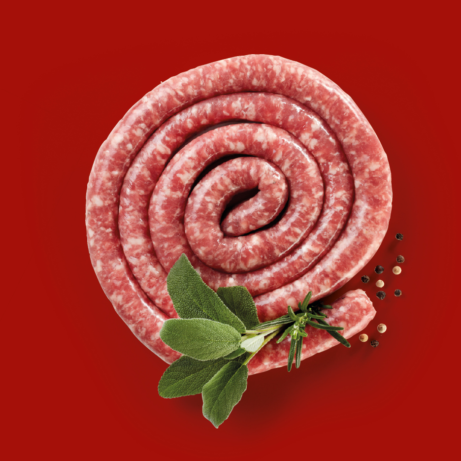 Salsiccia cruda a spirale con salvia, rosmarino e grani di pepe su sfondo rosso.