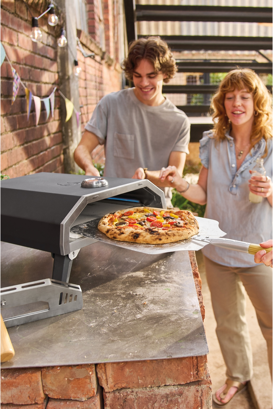 Un uomo e una donna preparano una pizza in un forno per pizza da esterno.