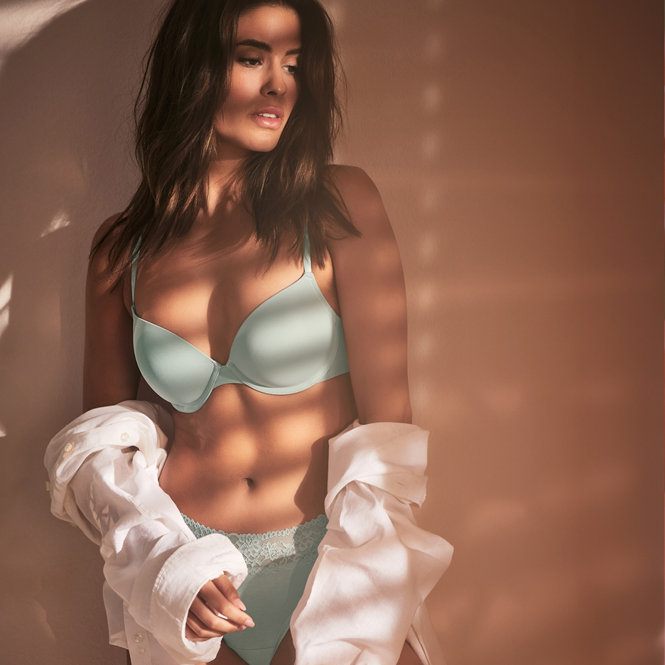 Una donna indossa un reggiseno e slip azzurri con una camicia bianca aperta.