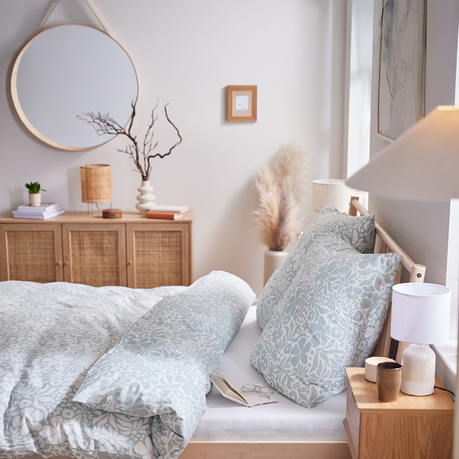 Camera da letto con letto in legno, biancheria da letto a fantasia blu e bianca, specchio rotondo e credenza in legno.
