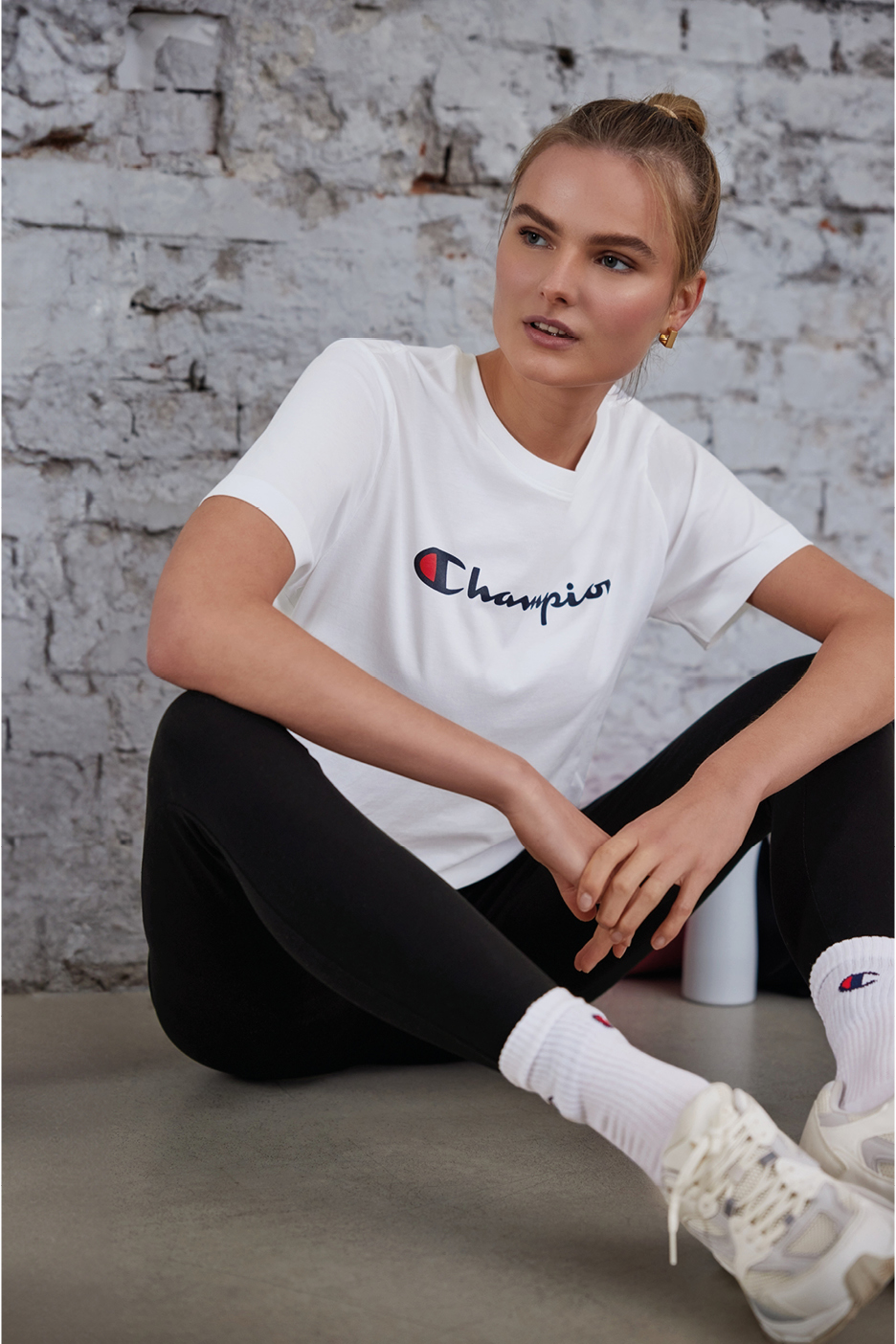 Donna in maglietta Champion bianca e leggings neri, seduta sul pavimento.