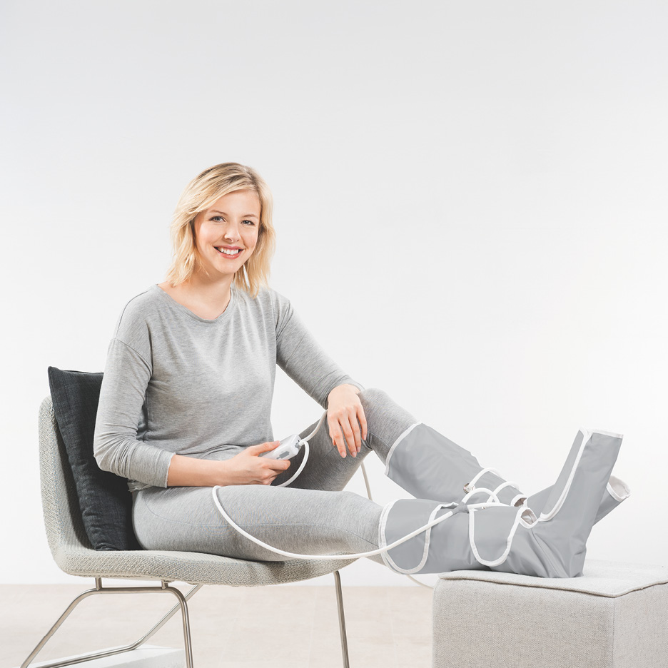 Donna seduta che utilizza un massaggiatore pressoterapico per gambe e piedi.