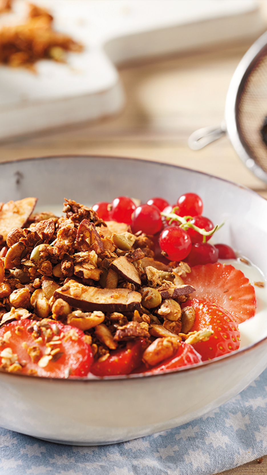 Ciotola di yogurt con granola, fragole e ribes rosso su un panno a quadri.