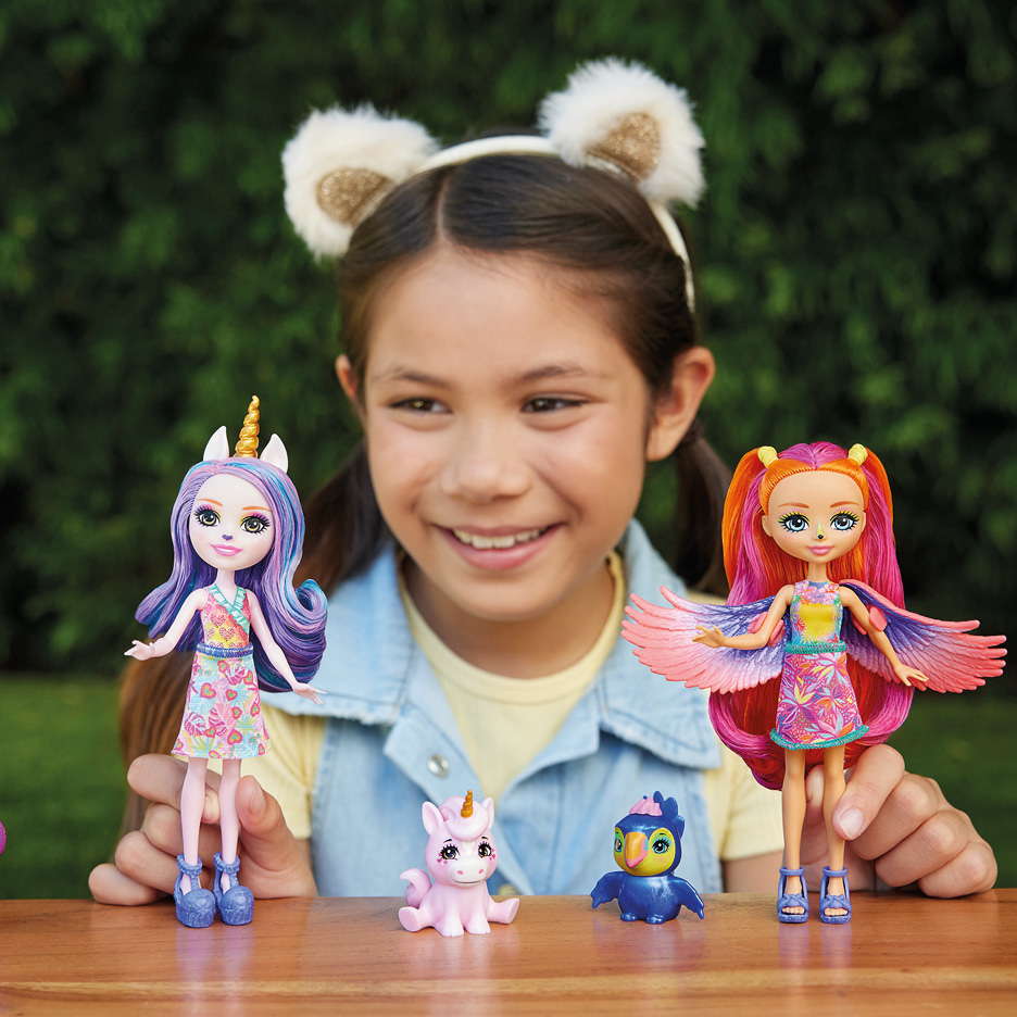 Bambina sorridente che gioca con bambole e piccoli personaggi colorati su un tavolo.