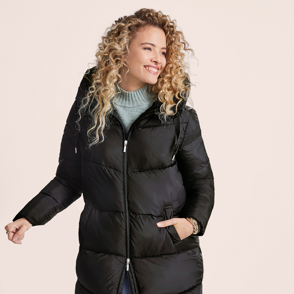 Donna sorridente con piumino nero e maglione a collo alto grigio.