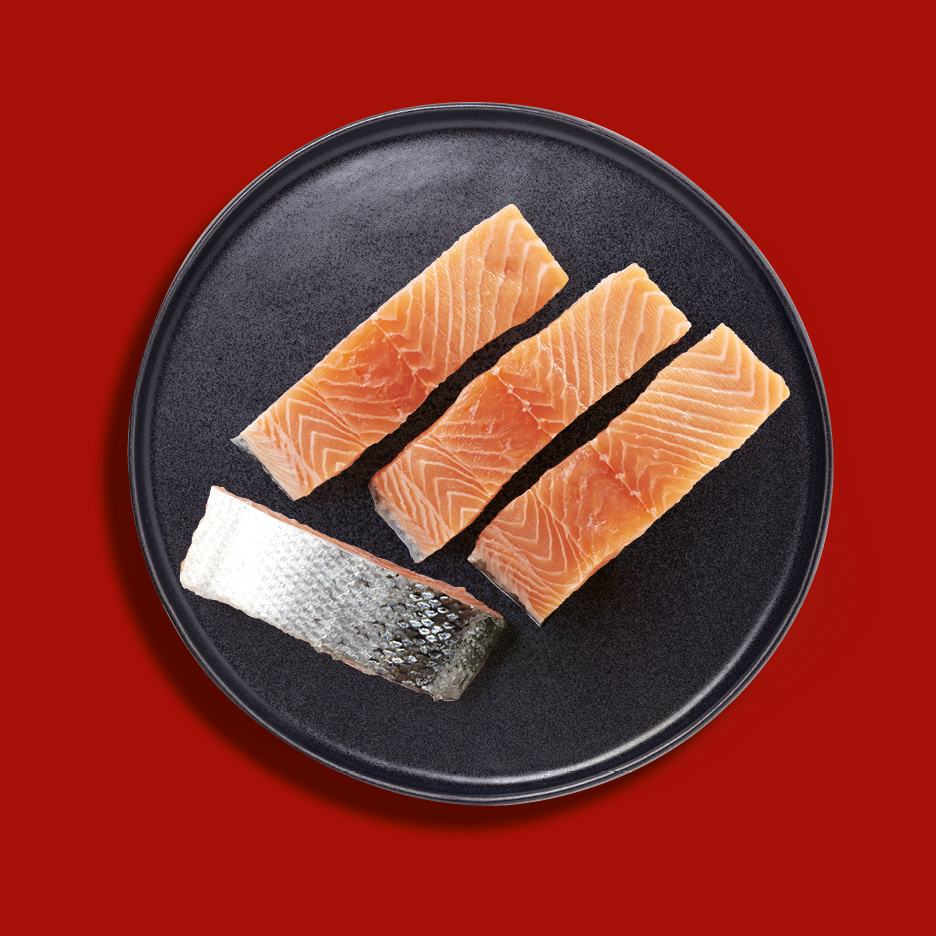 Quattro filetti di salmone crudo, uno con pelle, su un piatto nero.