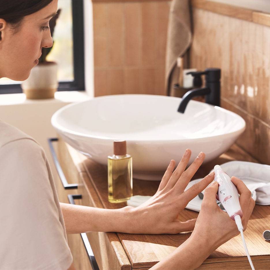 Donna che usa un set elettrico per manicure/pedicure su un mobile da bagno in legno con lavabo bianco.