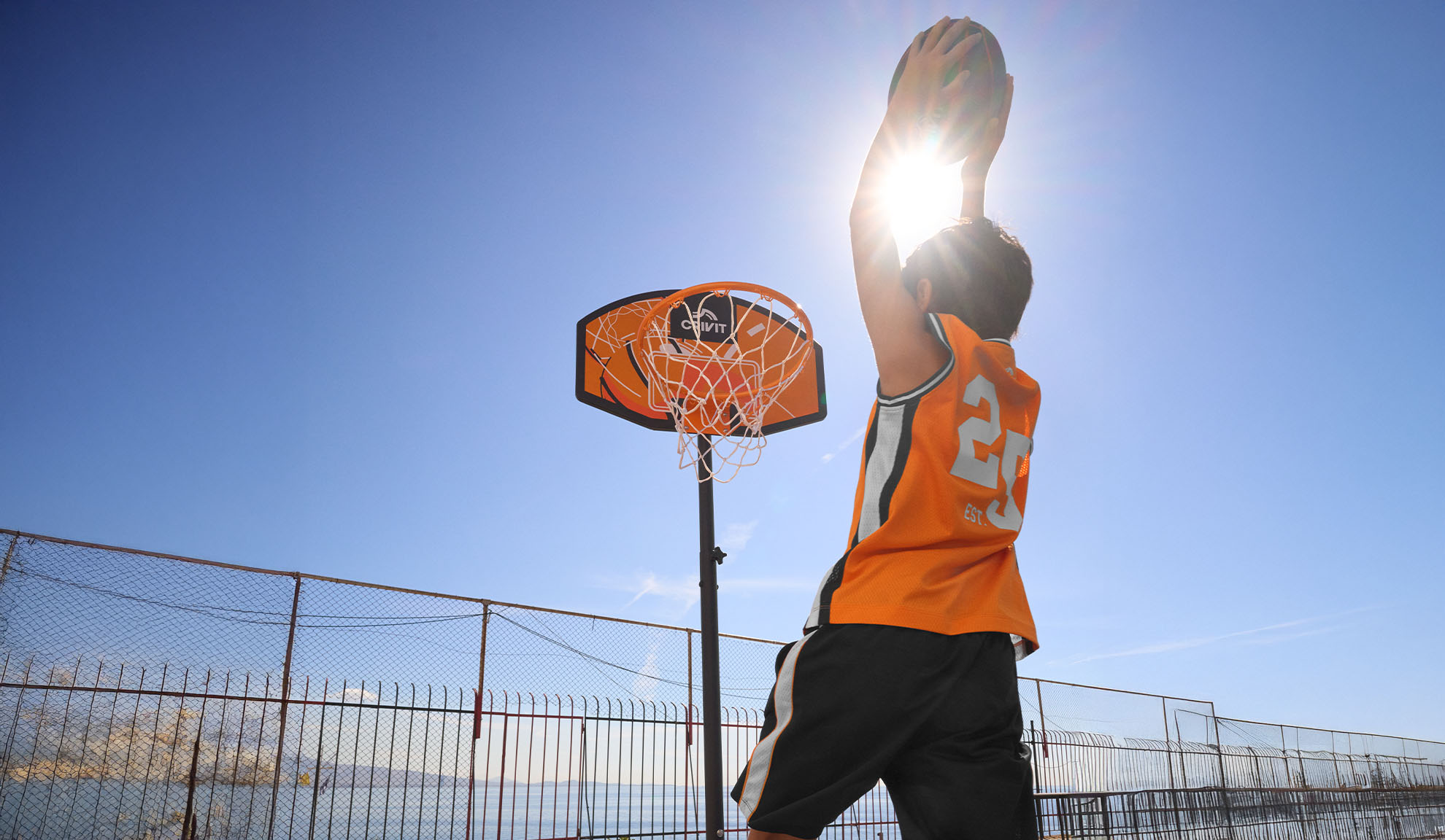 Ragazzo in maglia da basket che tira a canestro all'aperto sotto un sole splendente.
