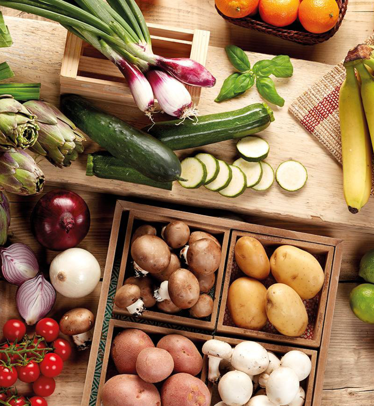 Verdure fresche assortite, tra cui cipolle, zucchine, carciofi, funghi e patate, su un tavolo di legno.