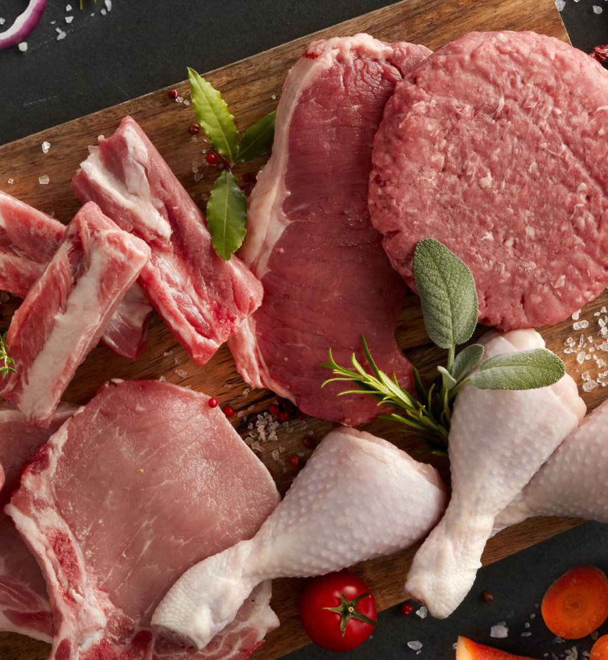 Assortimento di carne fresca su tagliere di legno: costolette, bistecche, hamburger, cosce di pollo.