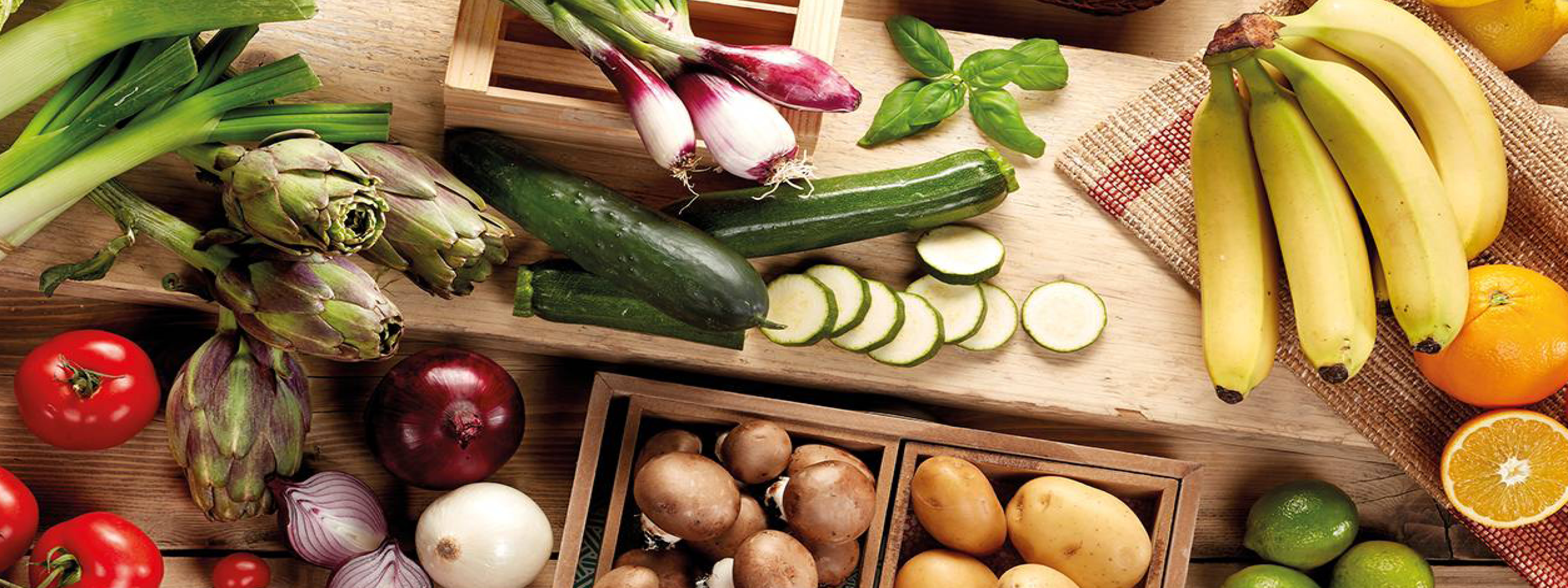 Verdure fresche assortite, tra cui cipolle, zucchine, carciofi, funghi e patate, su un tavolo di legno.