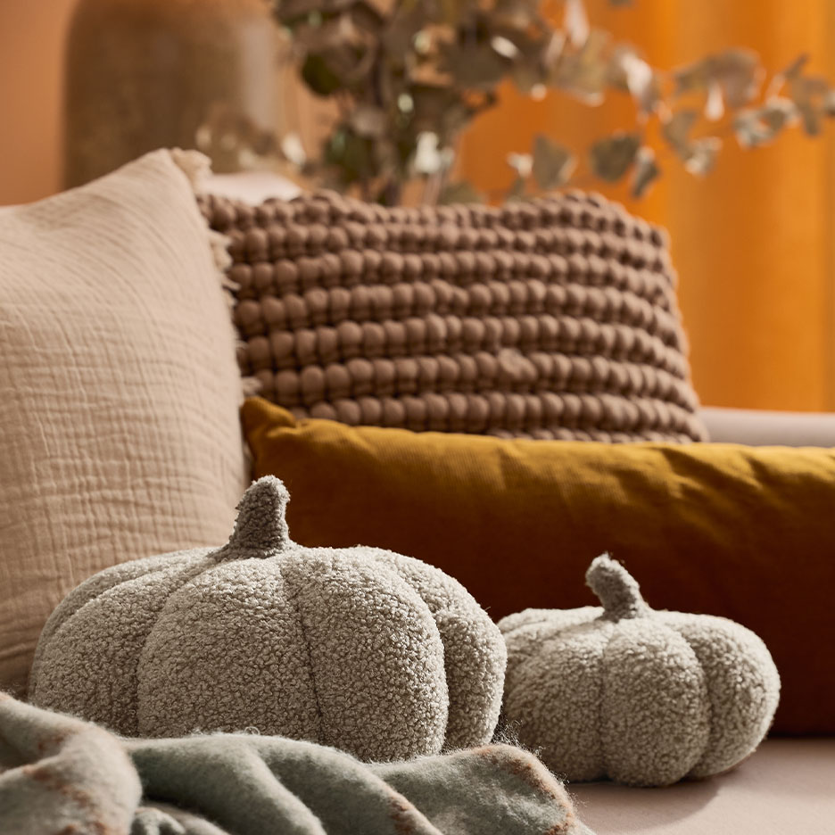Divano accogliente con cuscini decorativi e due morbidi cuscini a forma di zucca.