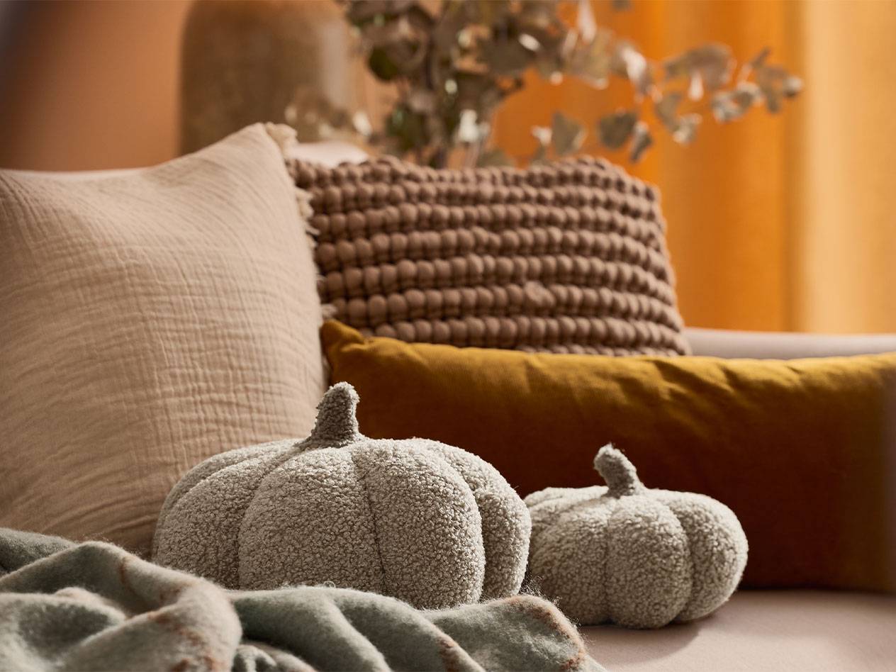 Due zucche decorative in peluche e cuscini in tonalità terrose su un divano.