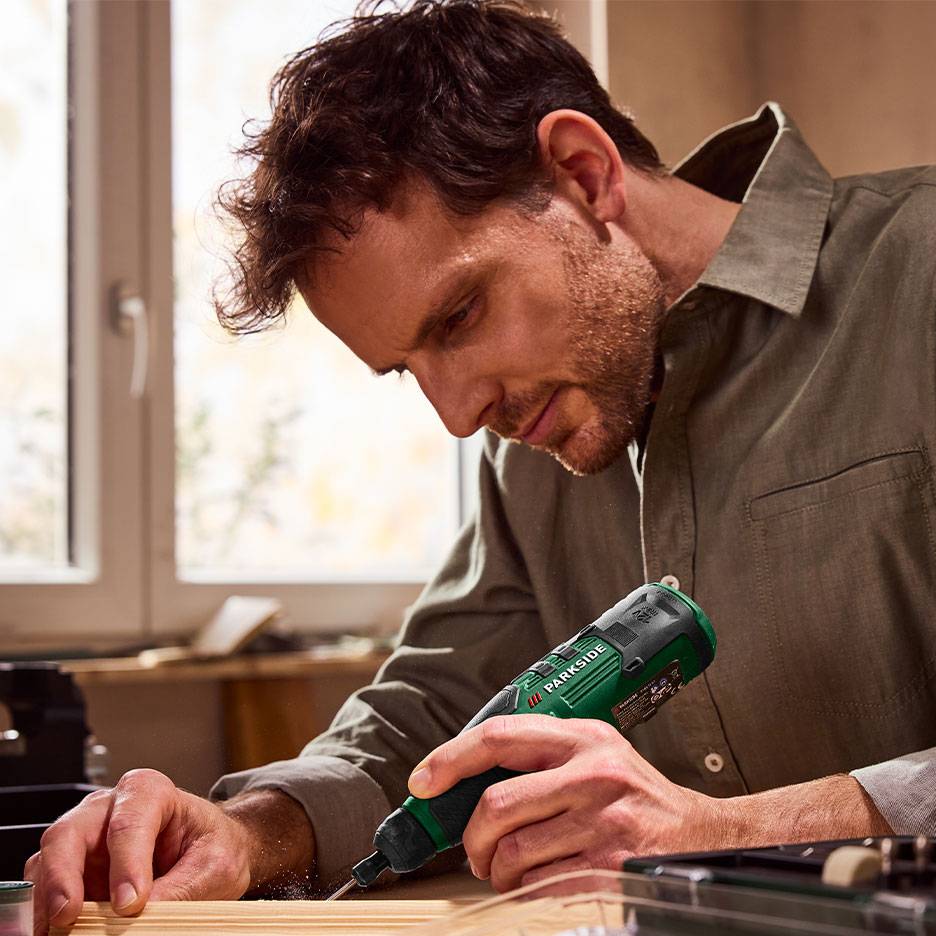 Uomo che usa un cacciavite elettrico verde per lavorare il legno.