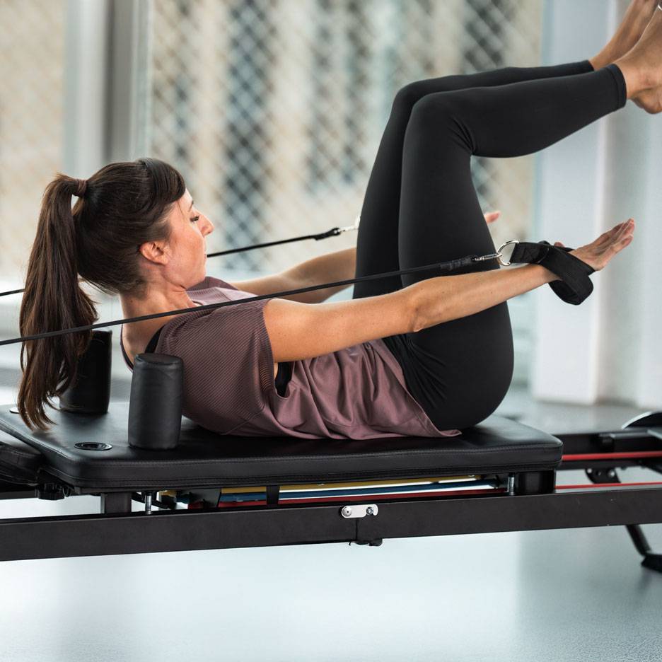 Donna che pratica Pilates su un reformer, indossando abbigliamento sportivo nero.