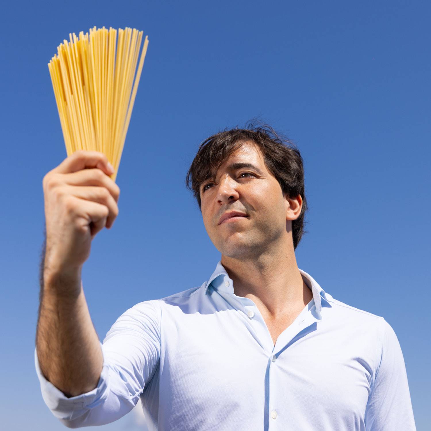 Uomo che tiene in mano un fascio di spaghetti, con il cielo blu sullo sfondo.