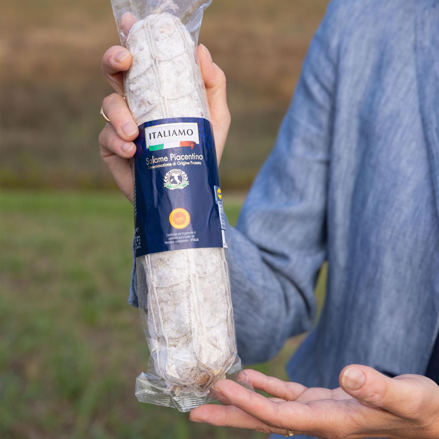 Mani che tengono una confezione di salame piacentino DOP.