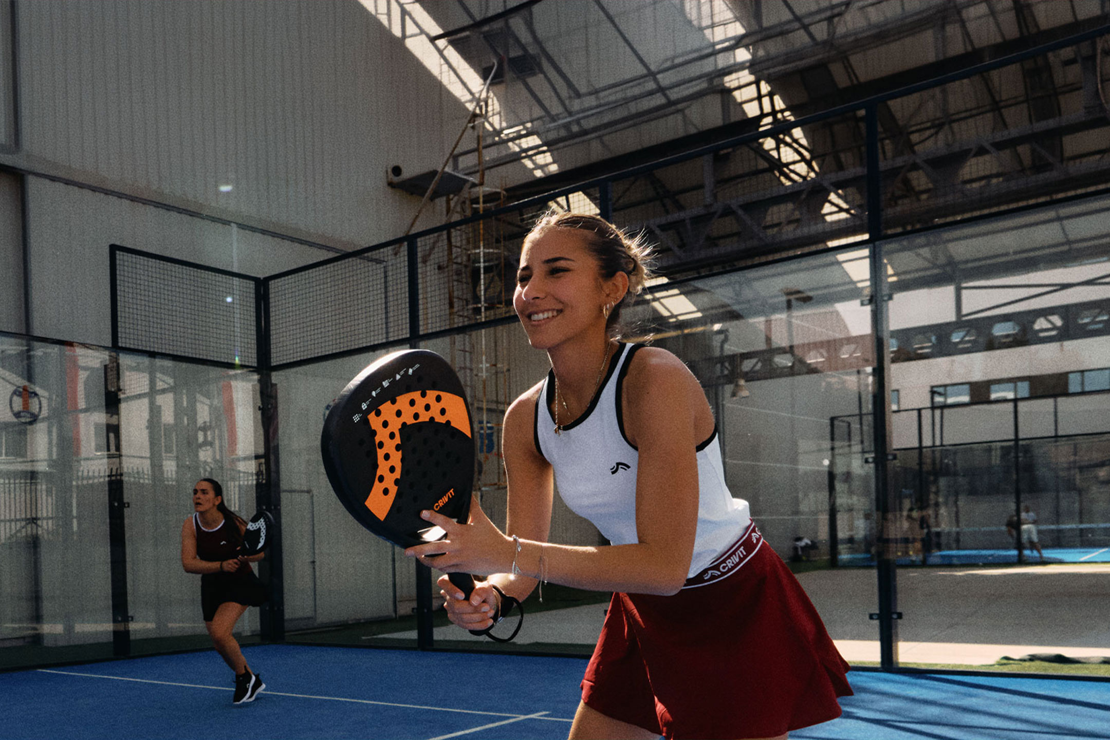undefined: Due donne giocano a padel, una sorride e tiene una racchetta, su un campo blu.