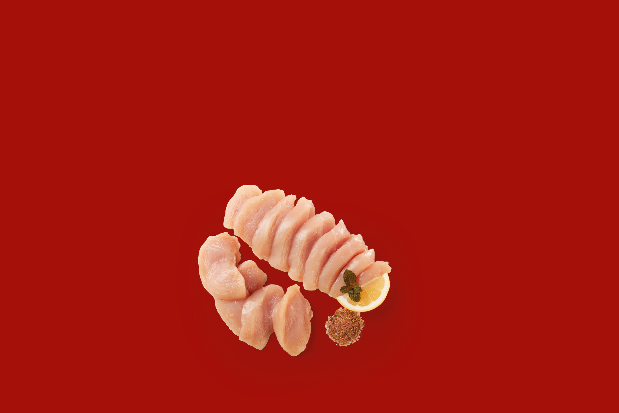 Fette di petto di pollo crudo con limone e spezie su sfondo rosso.