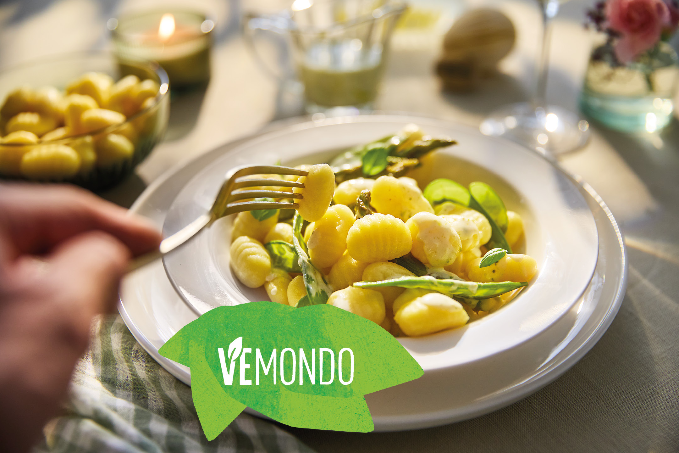 Gnocchi VEMONDO con asparagi e salsa, forchetta con uno gnocco, candela e bicchiere di vino