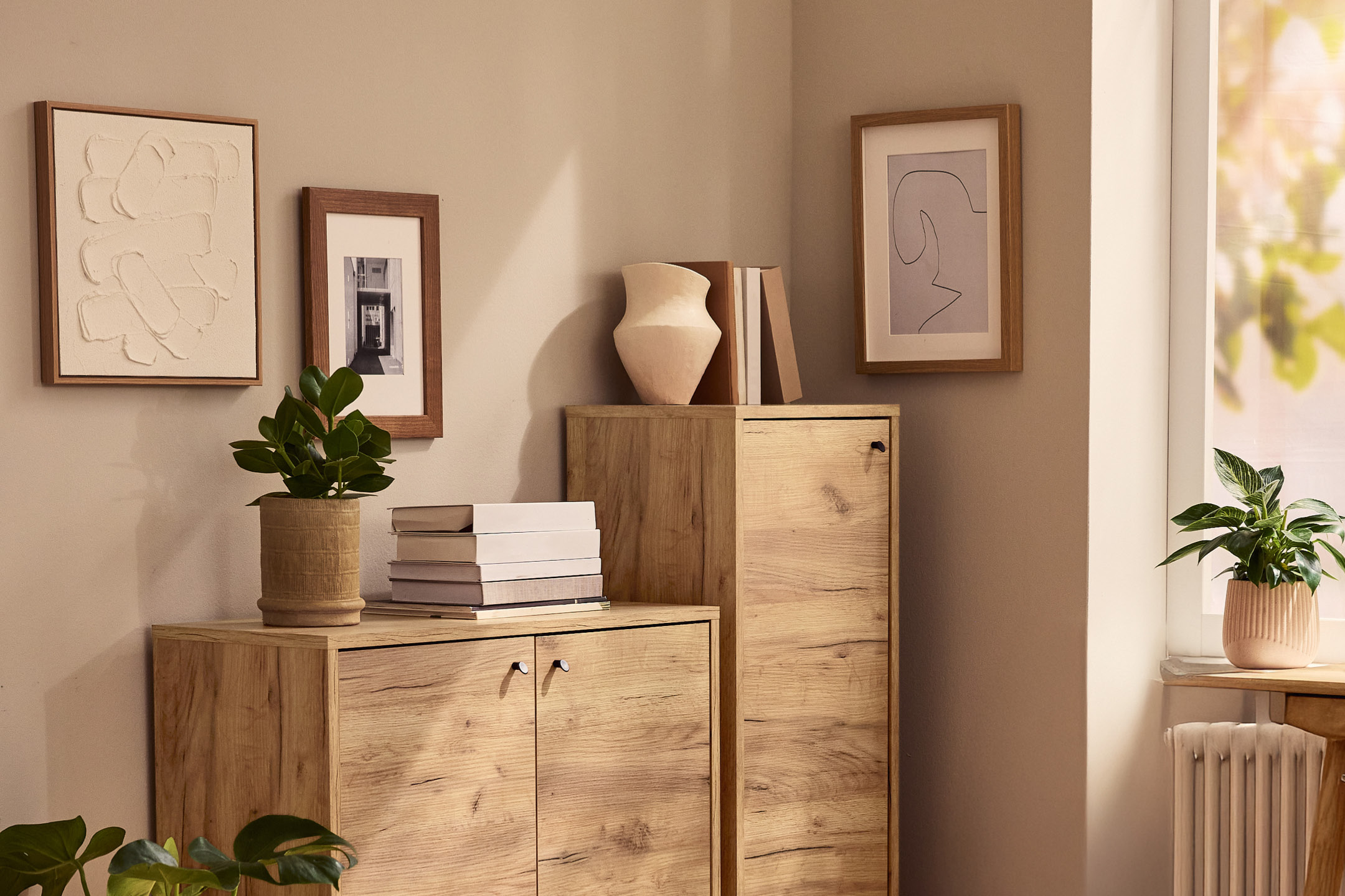 Mobiletti in legno chiaro con decorazioni e piante in vaso in un soggiorno luminoso.