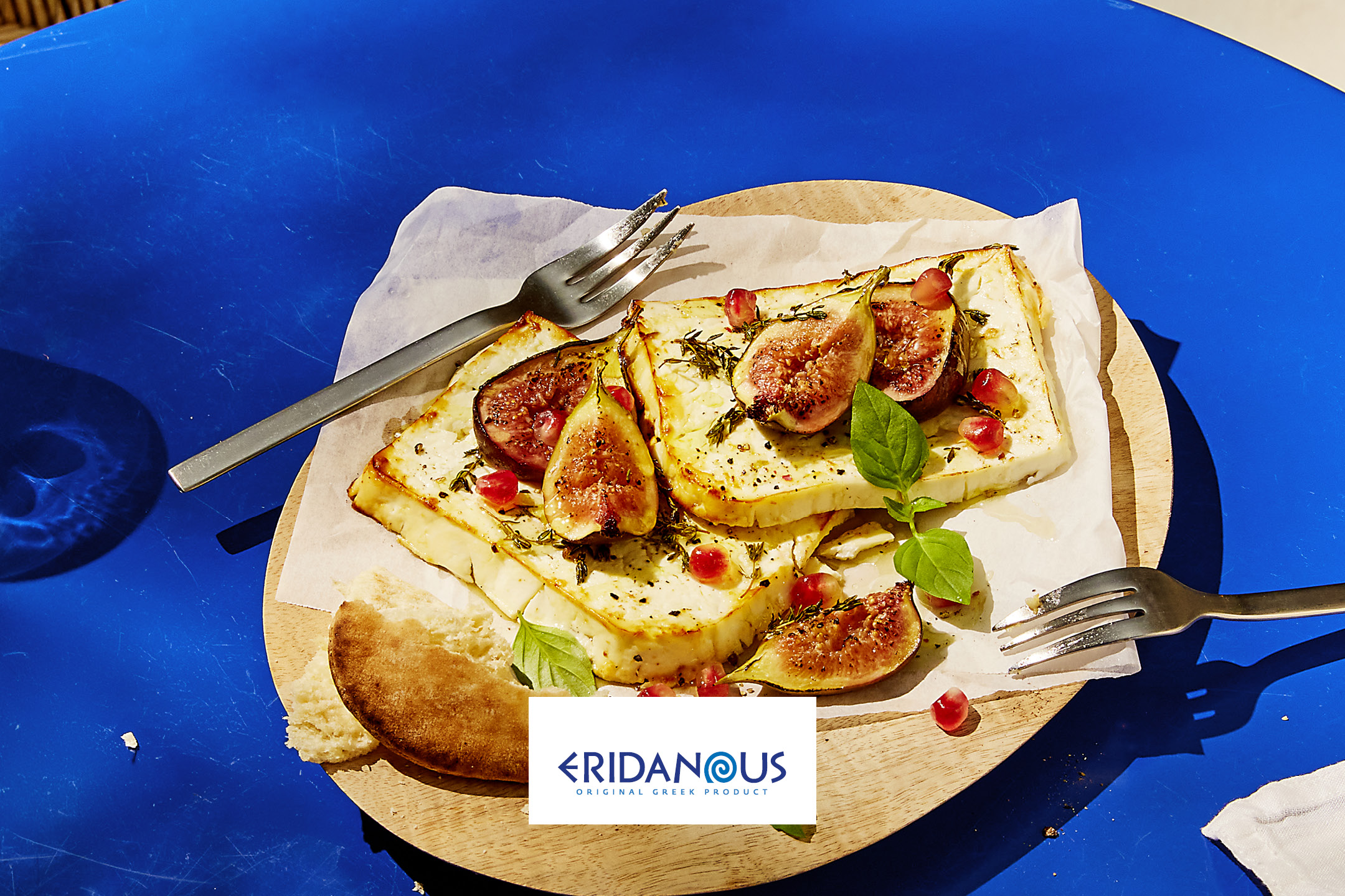 Formaggio greco Eridanous con fichi, melograno ed erbe aromatiche su un tagliere di legno.