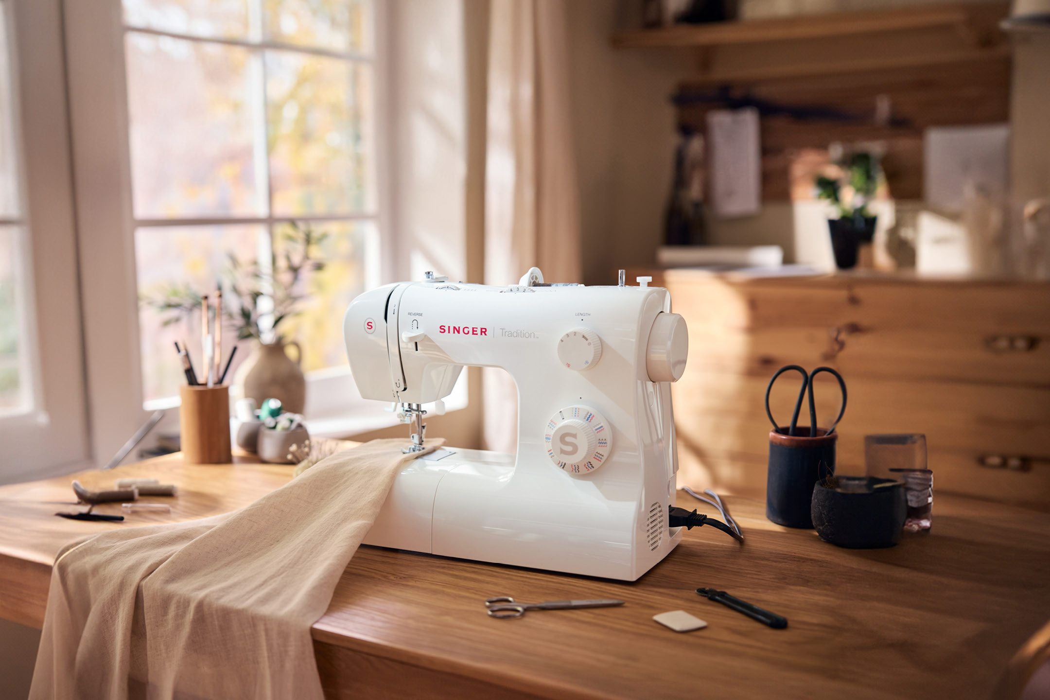 Macchina da cucire Singer Tradition su un tavolo di legno con tessuto e accessori.