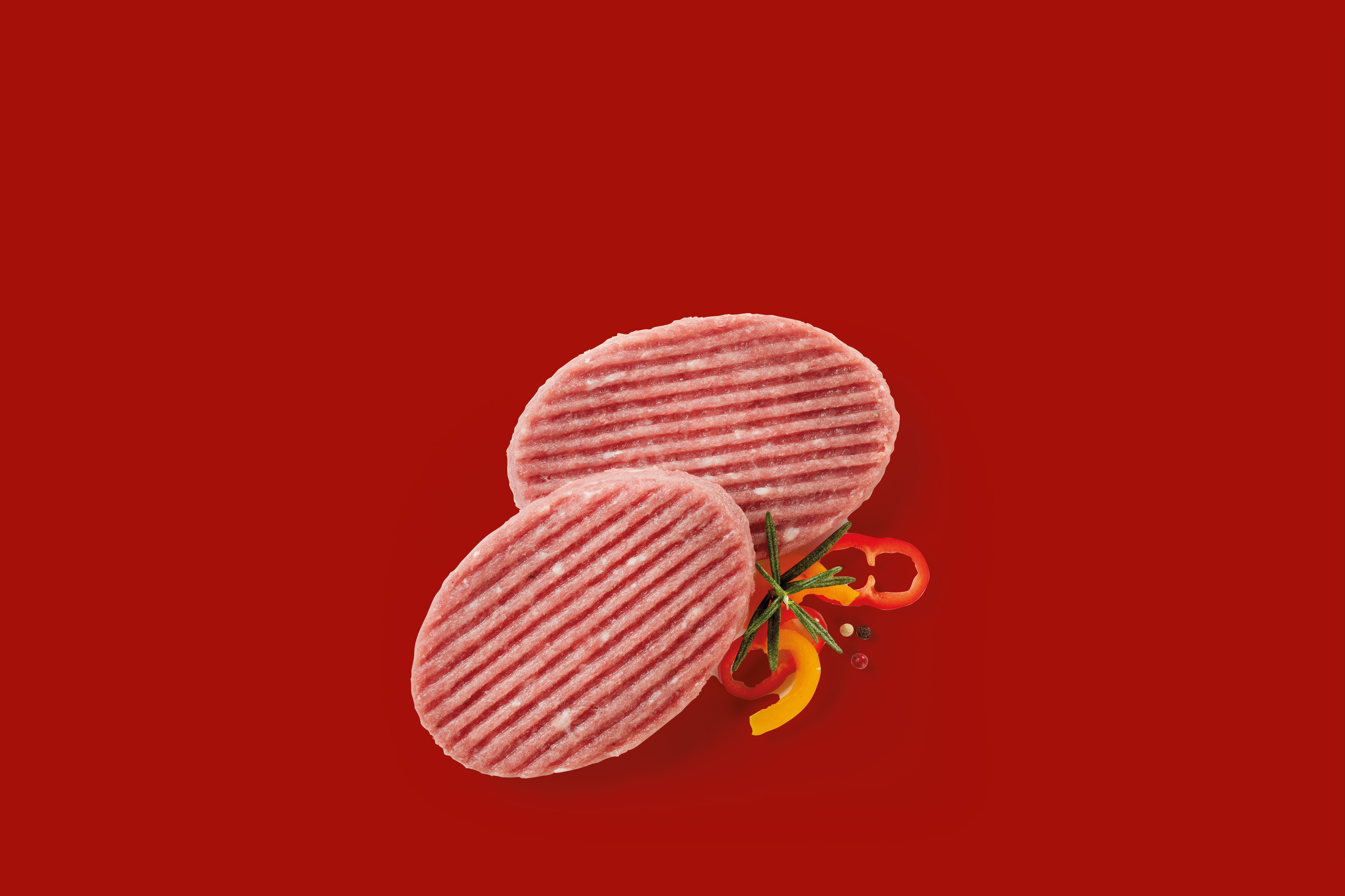 Due hamburger di carne cruda con rosmarino e peperoni su sfondo rosso.