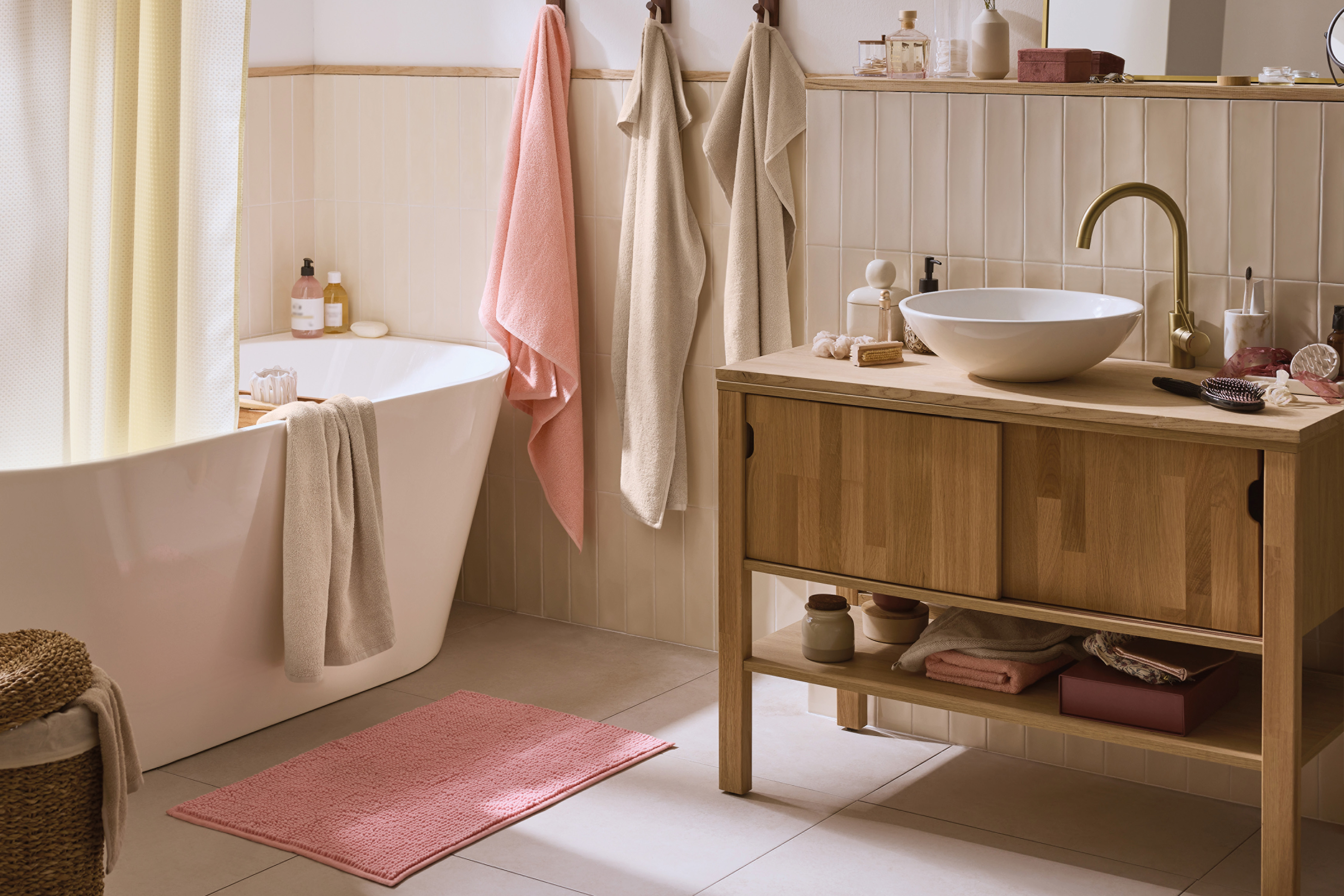 Bagno con vasca, mobile lavabo in legno, asciugamani rosa e beige, e tappeto rosa.