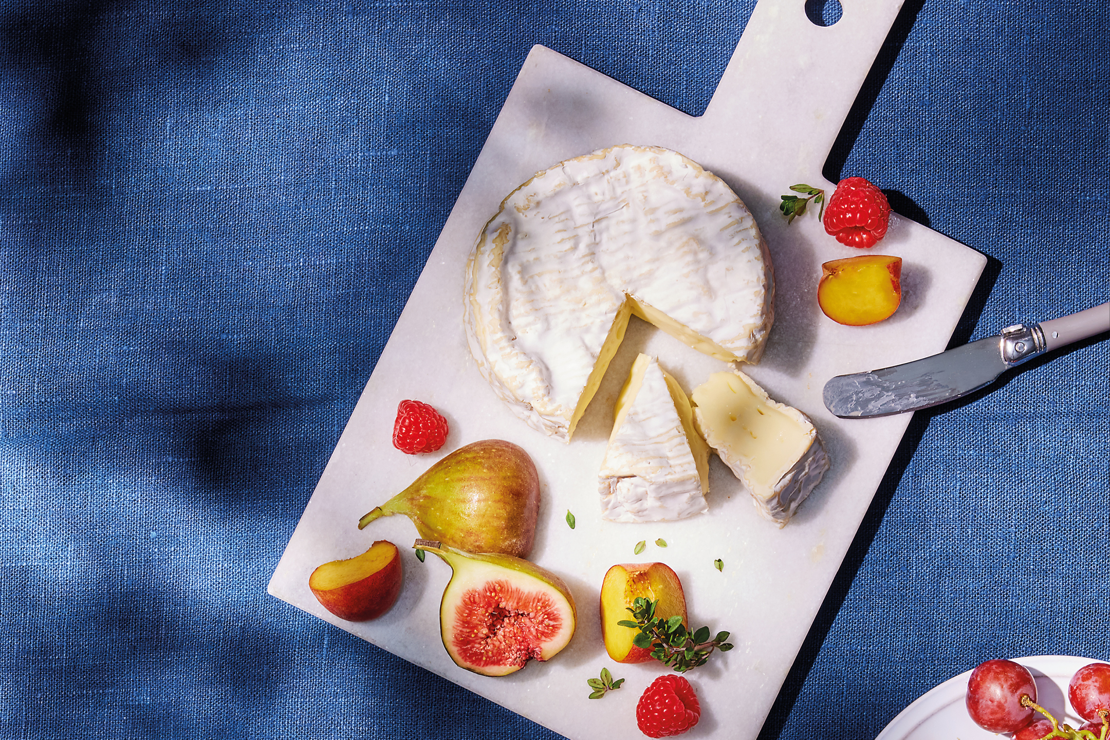 Formaggio brie con fichi, lamponi e pesche su un tagliere di marmo blu.