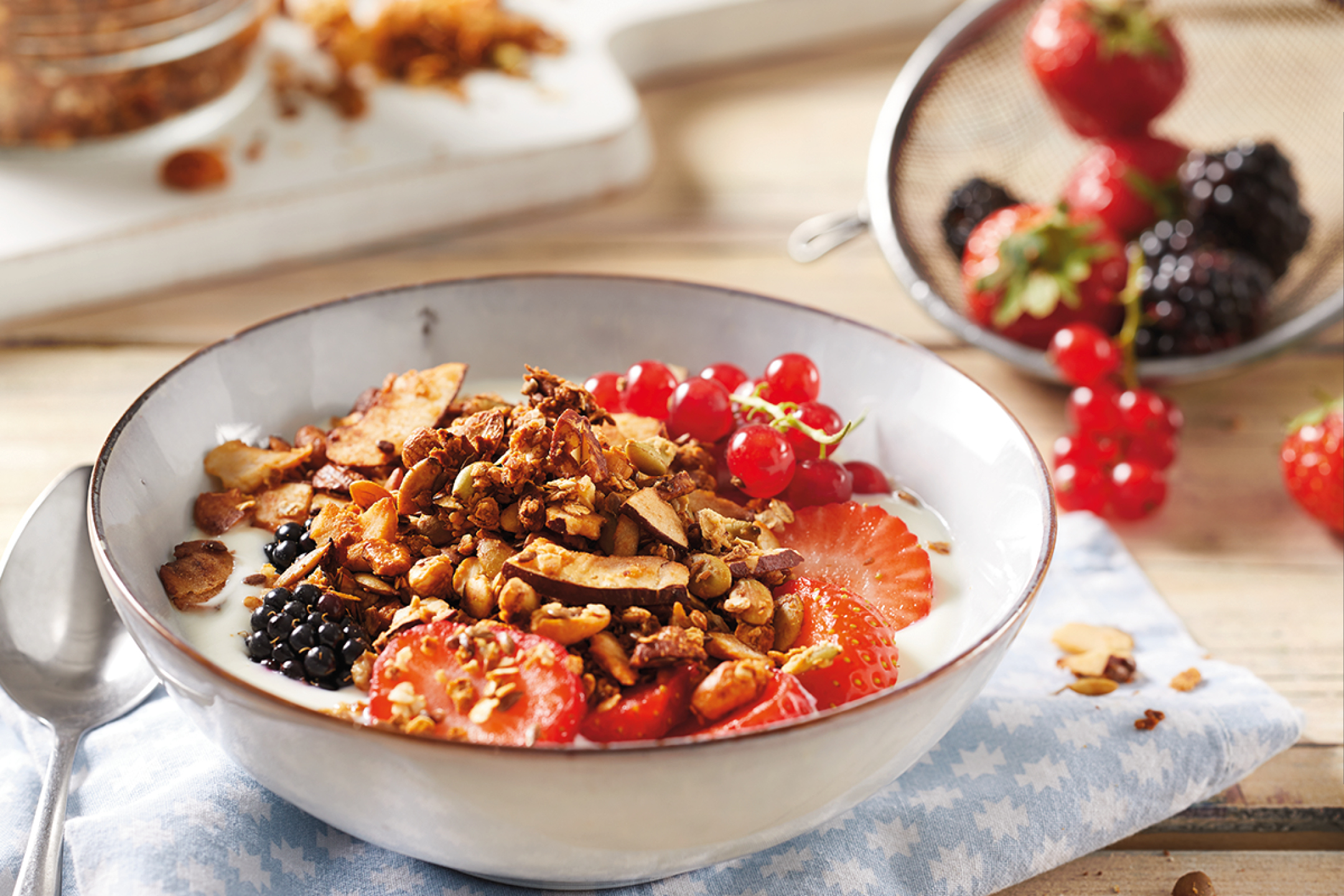 Ciotola di yogurt con granola, fragole, ribes rossi e more su un tavolo di legno.