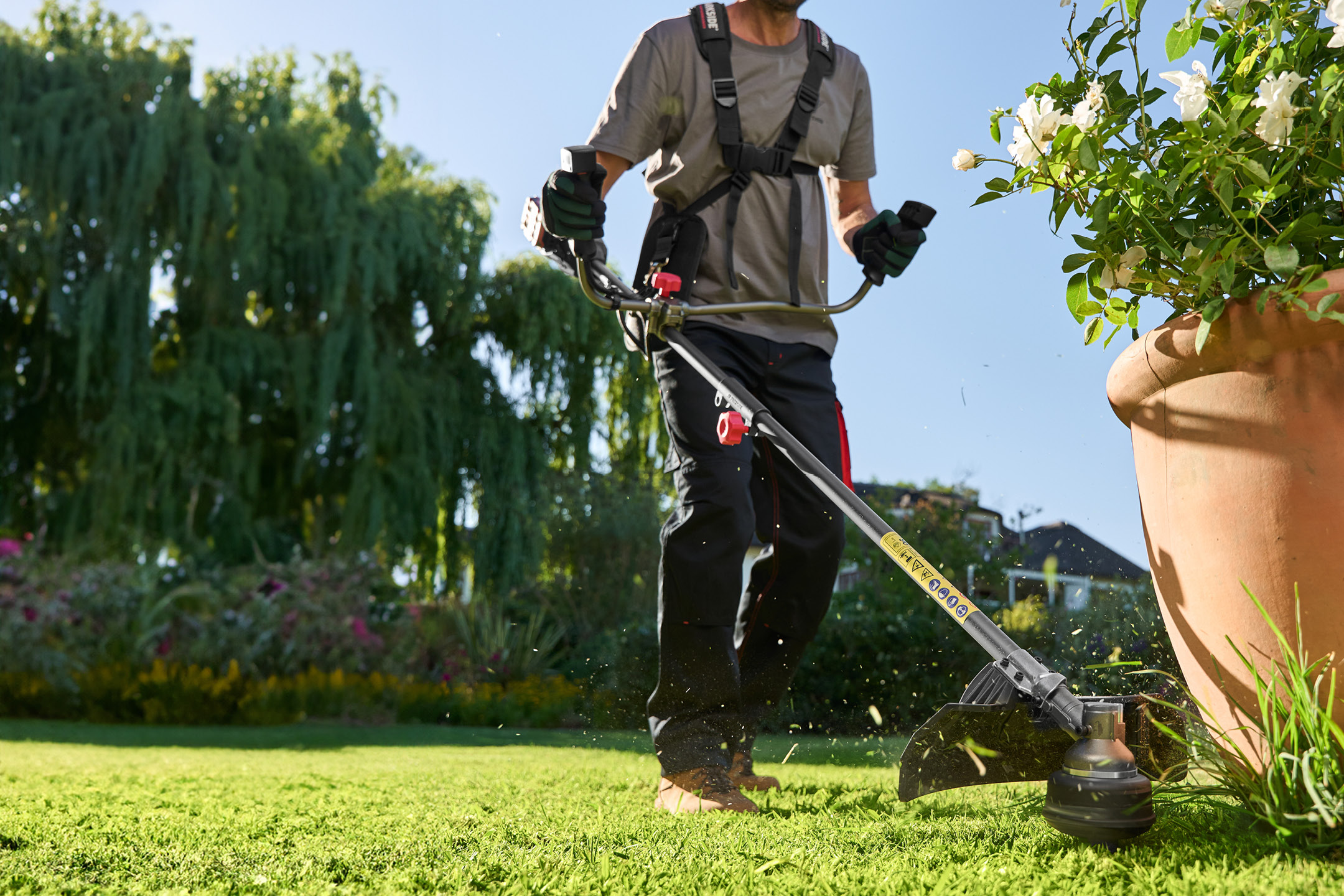 Uomo che taglia l'erba con un decespugliatore in un giardino soleggiato.