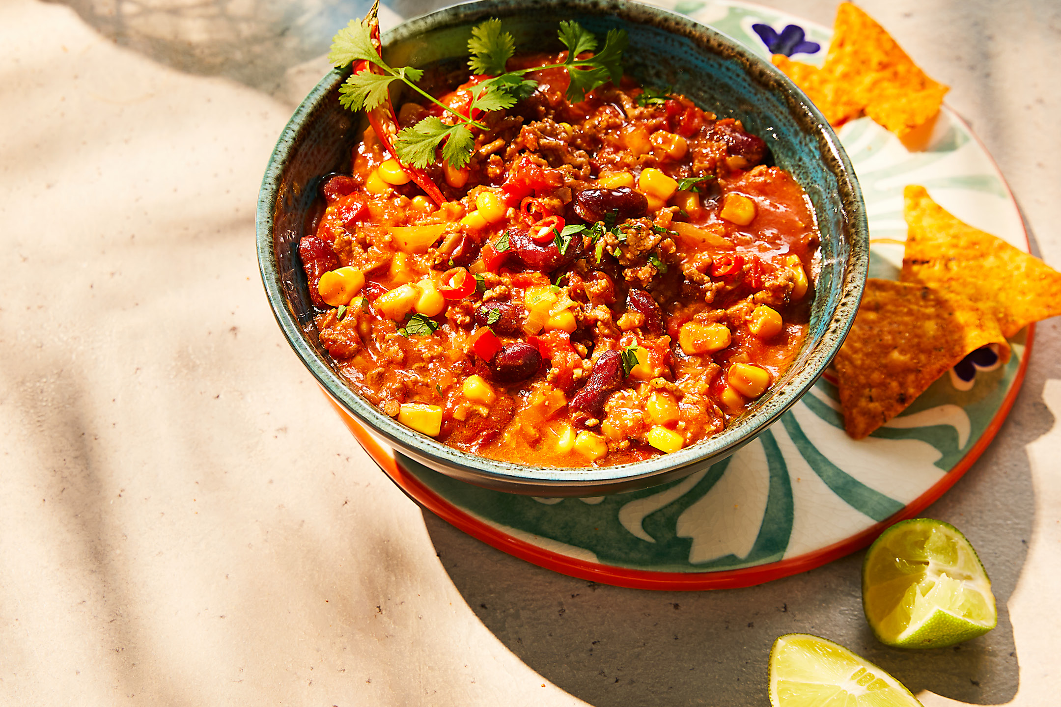Ciotola di chili con carne con mais, fagioli e coriandolo, accompagnata da nachos e lime.