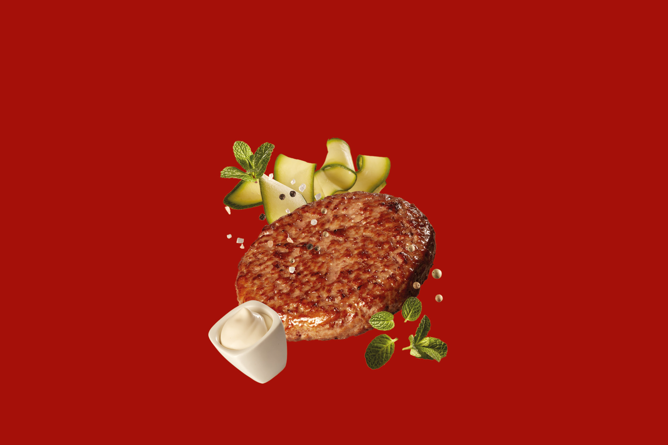Hamburger di manzo con zucchine, menta e salsa bianca su sfondo rosso.