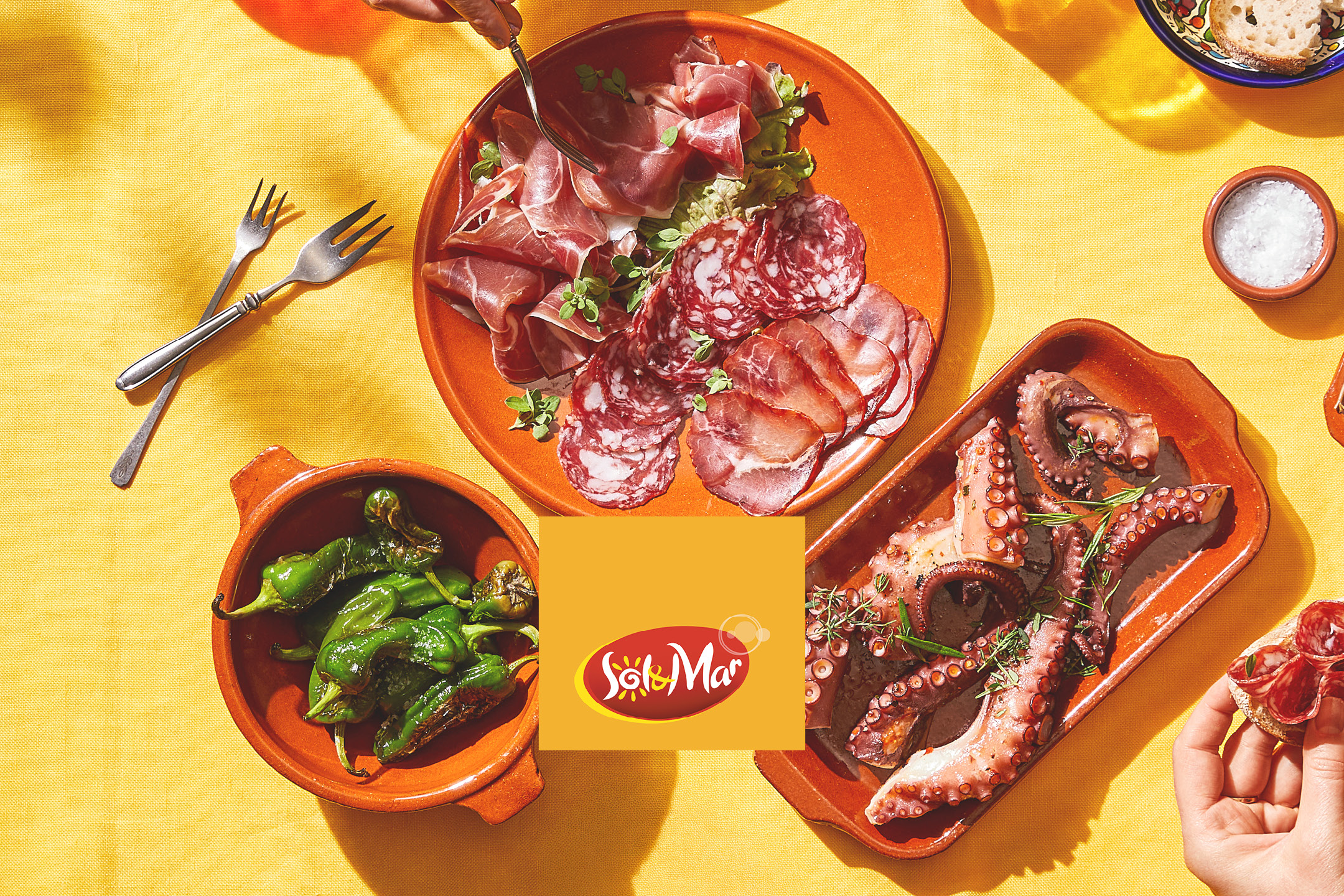 Tapas spagnole con salumi, polpo e peperoni su un tavolo giallo.