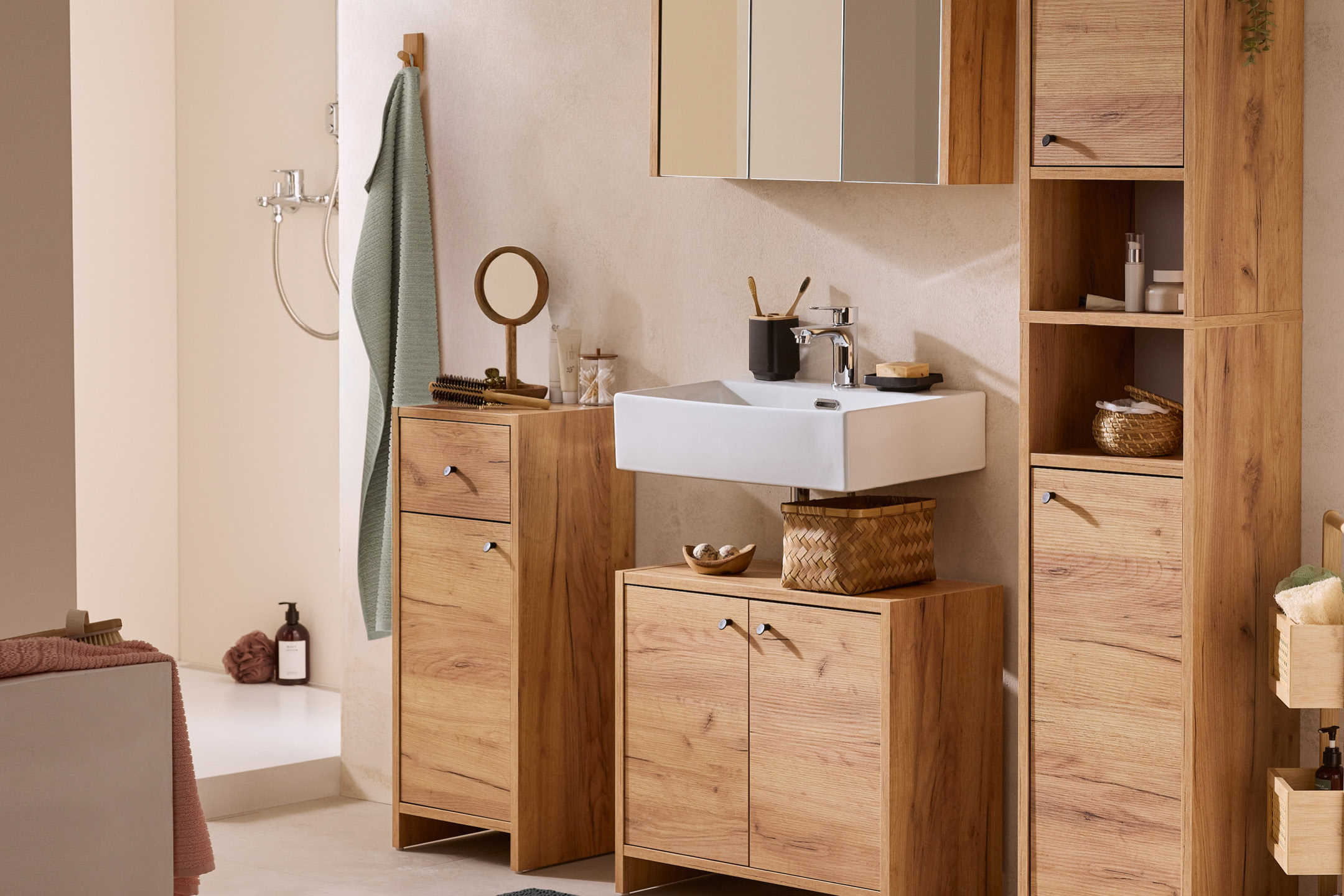 Bagno moderno con mobili in legno chiaro, lavabo bianco e accessori coordinati.