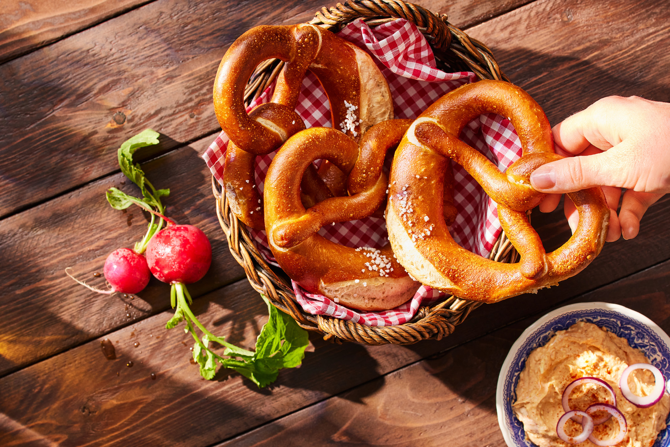 Pretzel salati in un cesto, con ravanelli e una ciotola di spalmabile al formaggio.