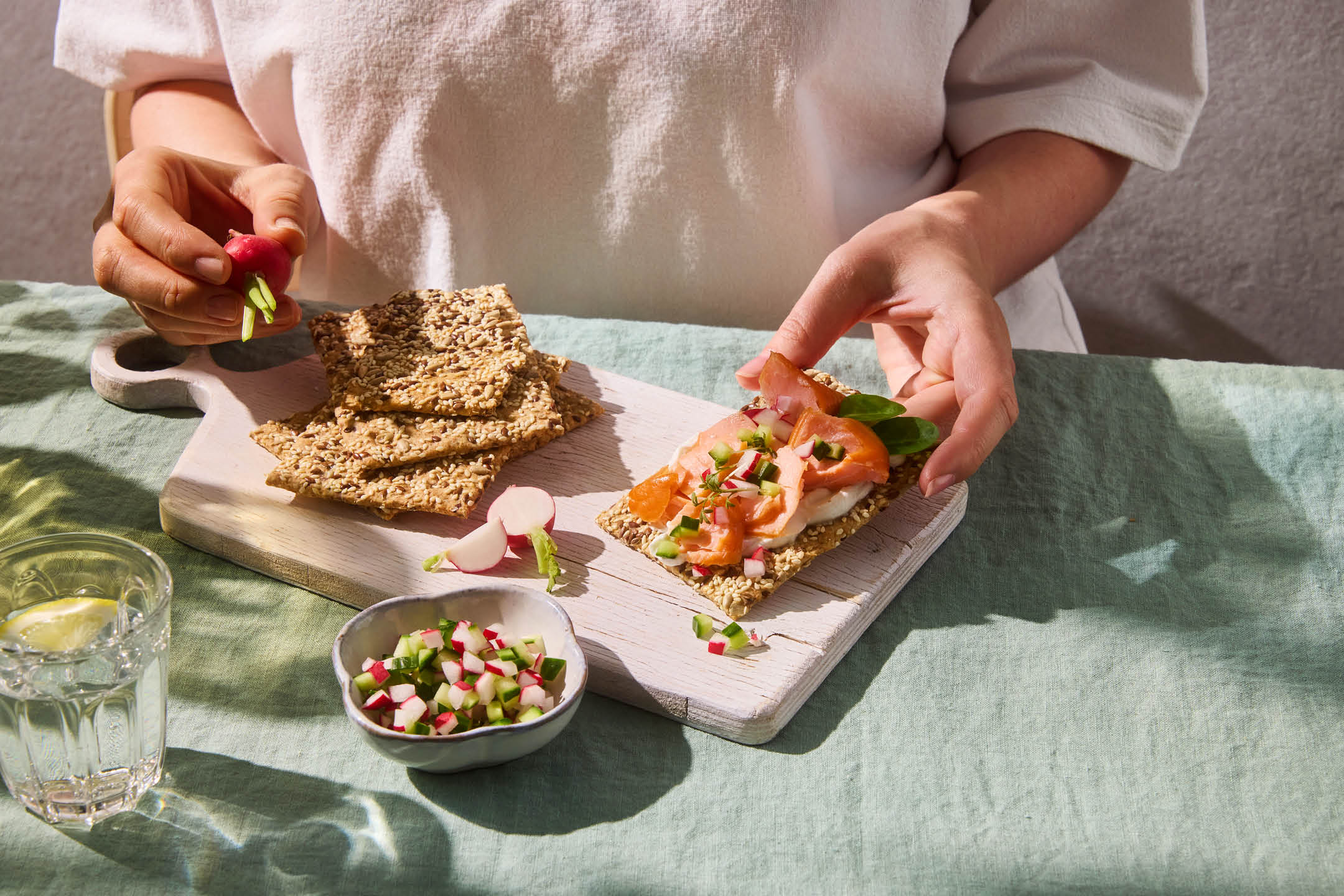 Persona che prepara cracker di semi con salmone affumicato, formaggio spalmabile e ravanelli.
