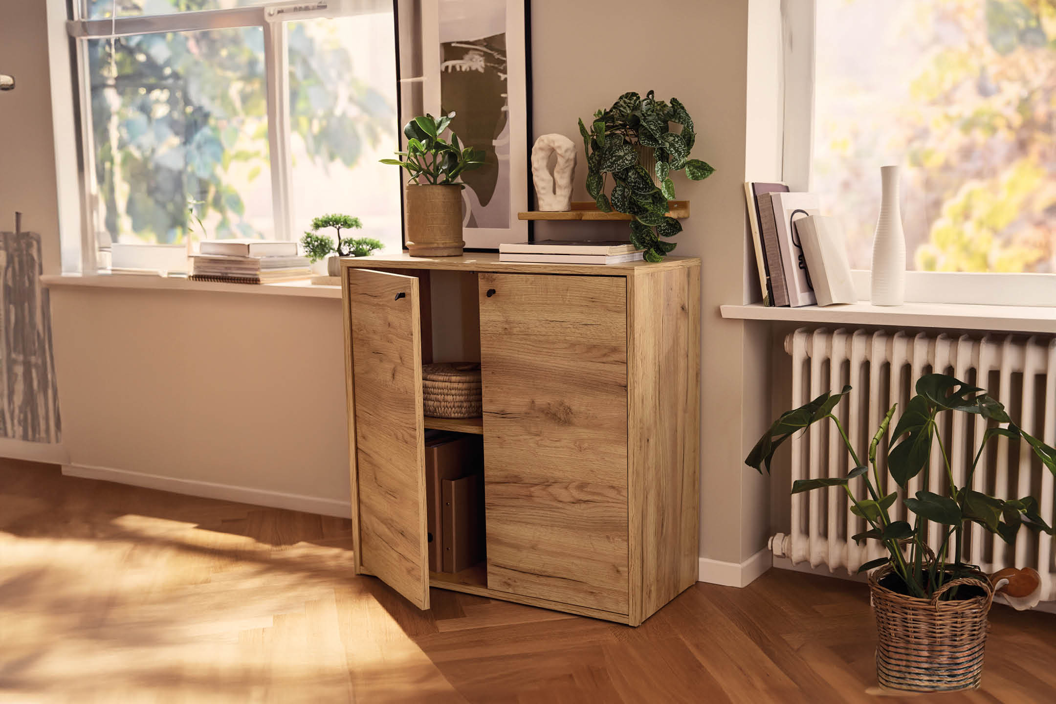 Mobiletto in legno chiaro con ante aperte, decorato con piante e libri, in un ambiente luminoso.