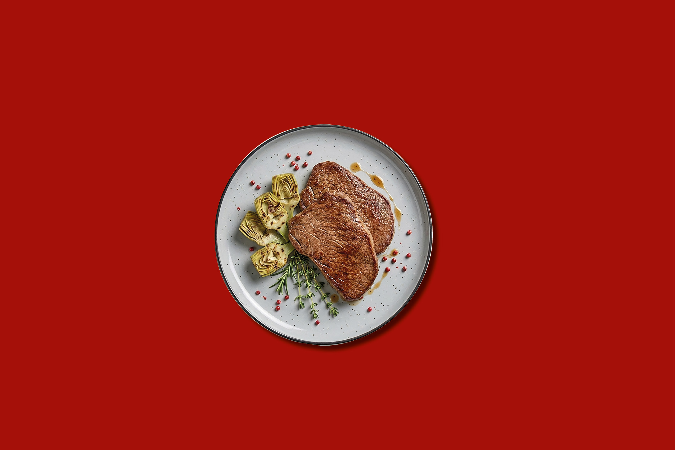 Bistecche di manzo con carciofi e rosmarino su un piatto bianco.