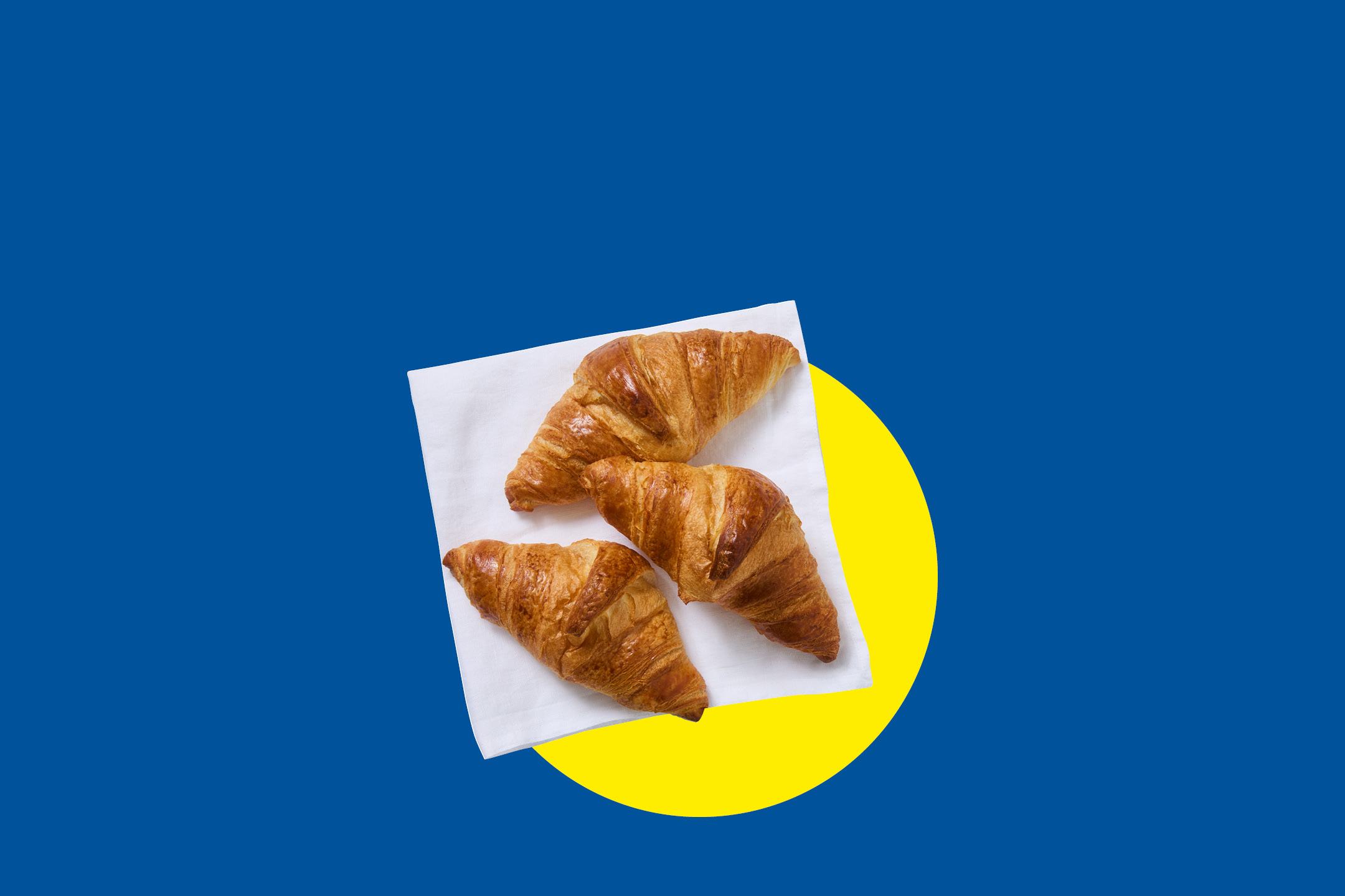 Tre croissant dorati su un tovagliolo bianco, su sfondo blu e cerchio giallo.