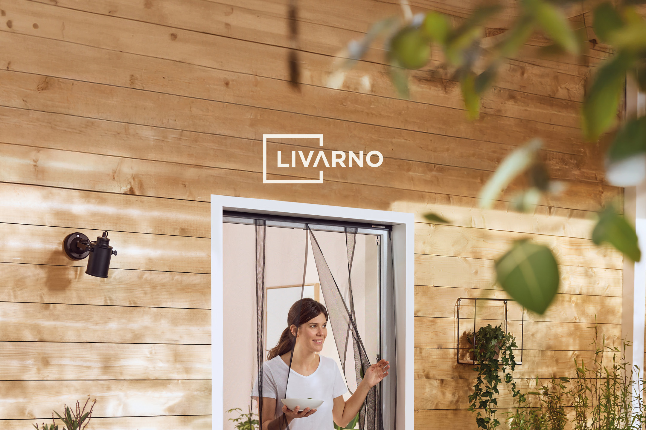 Donna sorridente con zanzariera magnetica per porta, su sfondo di parete in legno.