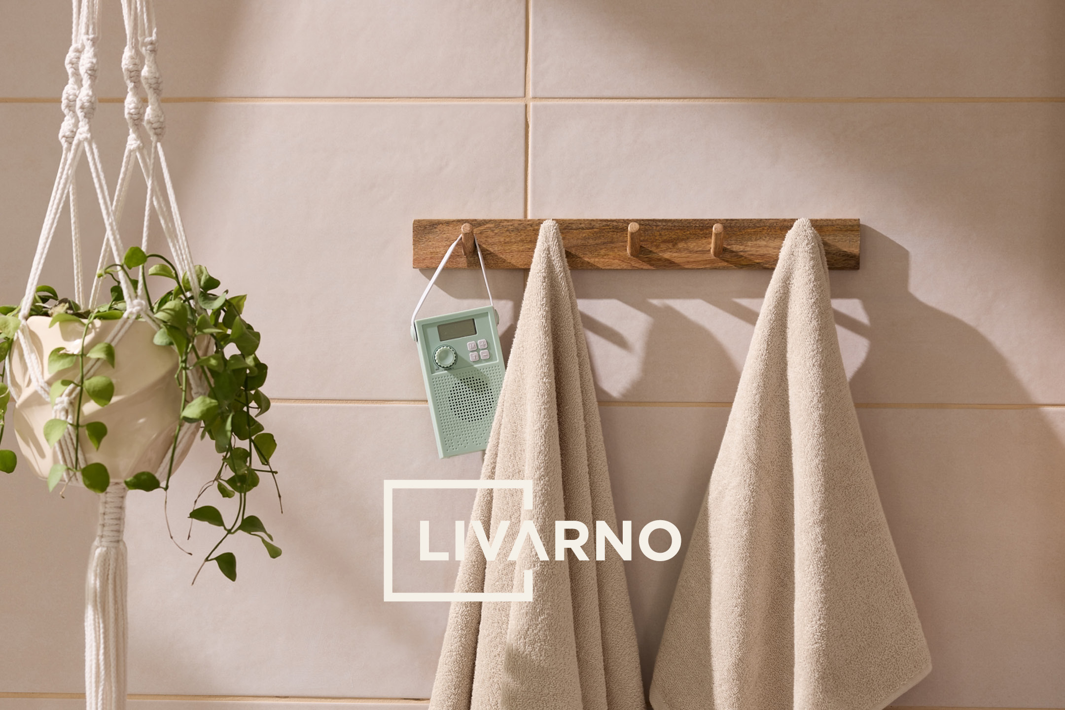 Asciugamani beige su appendiabiti in legno, con pianta in vaso e radio, su piastrelle chiare.