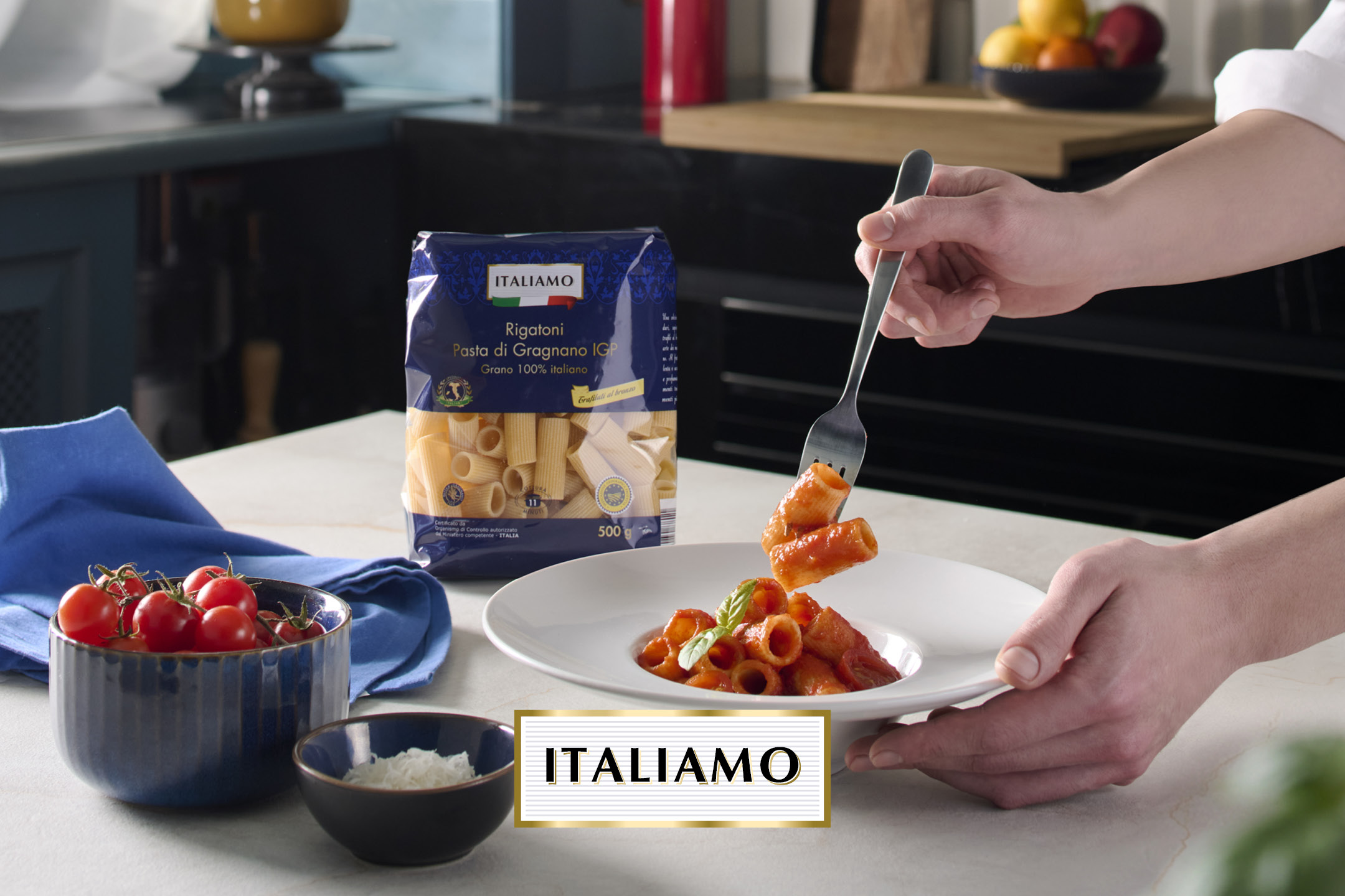 Pasta rigatoni con sugo, pomodorini e formaggio, con confezione di pasta sullo sfondo.